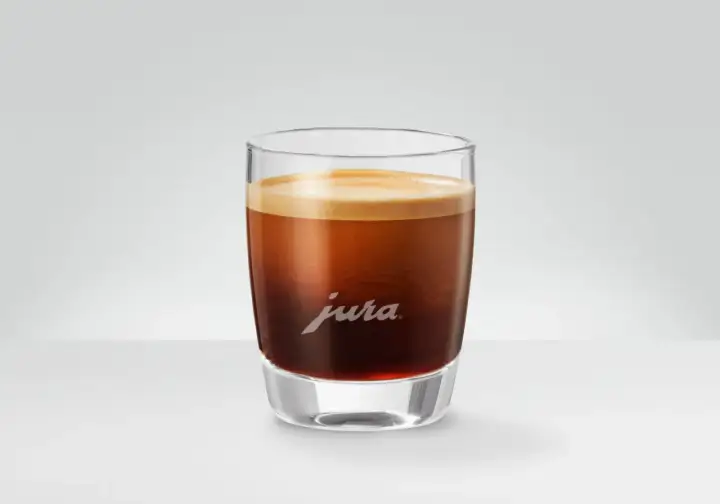 En perfekt dubbel espresso med gyllene crema i ett elegant glas med Jura-logotypen.
